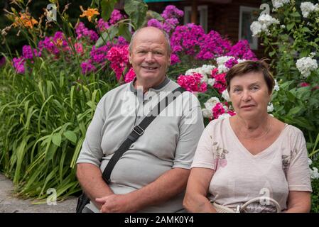 Porträt eines hochrangigen russischen Paares im Park in Sibirien mit hellen Blumen im Hintergrund. Stockfoto