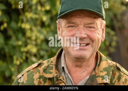 Nahaufnahme des Porträts eines lächelnden russischen Mannes, der eine grüne Kappe und eine Tarnjacke trägt. Stockfoto