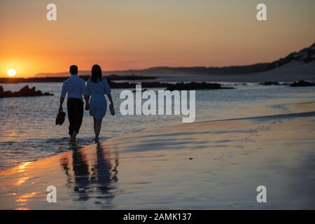 Ein Paar, das bei Sonnenuntergang am Strand spazieren geht Stockfoto