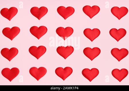 Valentinstag. Glatte, gleichmäßige Reihen roter Herzen auf einem rosafarbenen Hintergrund. Flaches Lay. Draufsicht. Minimales Konzept. Stockfoto
