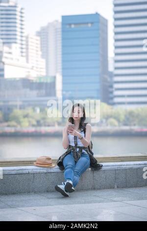 Schöne asiatische Touristenfrau, die sich entspannt und die Musik auf einem Smartphone in der Innenstadt hört. Urlaub im Sommer. Stockfoto