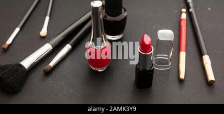 Kosmetikprodukte in Rot und Schwarz herstellen. Roter Lippenstift und nagellack, Augenstift und Bürsten vor schwarzem Farbhintergrund Stockfoto