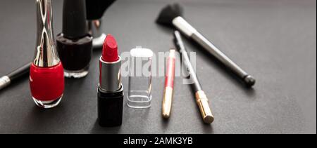 Kosmetikprodukte in Rot und Schwarz herstellen. Roter Lippenstift und nagellack, Augenstift und Bürsten vor schwarzem Farbhintergrund Stockfoto