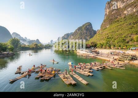 Yangshuo, Guilin, Provinz Guangxi, China - 9. November 2019: Touristische Bambusflöße, die am Ende der Tour auf dem Fluss mit karstigen Kalkhügeln und blauem Himmel im Hintergrund ankommen. Stockfoto