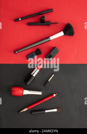 Kosmetikzubehör in rot und schwarz aufmachen. Lippenstift, nagelpoliermittel, Augenstift und Bürsten vor rotem und schwarzem Farbhintergrund Stockfoto