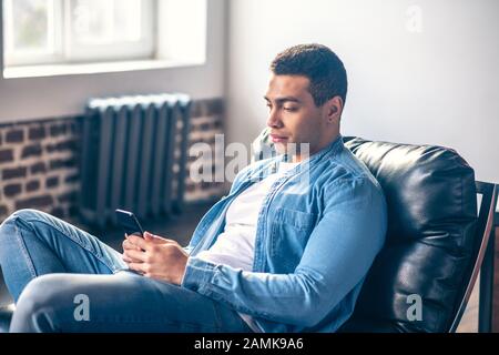 Junger Mann im Stuhl mit Smartphone in den Händen. Stockfoto