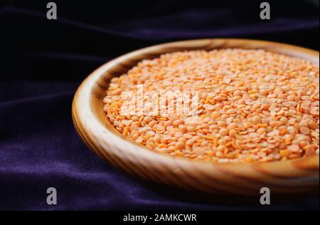 Nahaufnahme einer Holzschale mit roten Linsen (Lens culinaris) gegen einen dunklen Background mit Kopierraum. Selektiver Fokus. Stockfoto