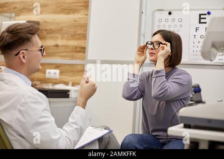 Porträt der aufgeregten jungen Frau, die neue Brille in der Klinik für Augenheilkunde aufsetzt, Kopierer Stockfoto