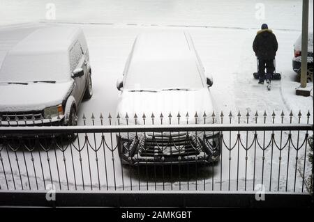 Autos bedeckt mit Schnee auf der Straße und ein Mann remiving Schnee im Hintergrund Stockfoto