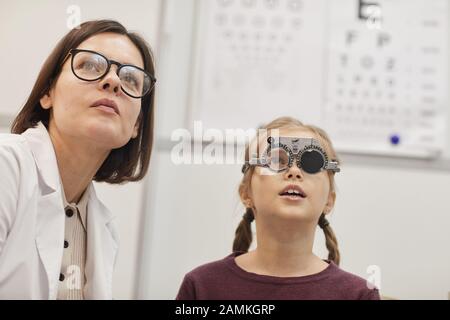 Portrait von niedlichem Mädchen im Teenager-Alter, das während des Childs Vision-Tests in der modernen Augenklinik einen Testrahmen trägt, Copy-Space Stockfoto