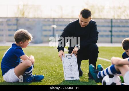 Young Soccer Trainer Coach Erklärt Taktik im Team Sports Tactics Board. Kinder Während Der Fußball-Coaching-Sitzung. Jungen in der Liste der Fußballmannschaften Stockfoto