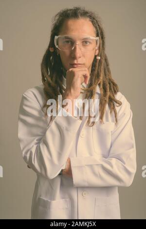 Junger Mann Doktor mit Dreadlocks trägt Schutzbrille vor grauem Hintergrund Stockfoto