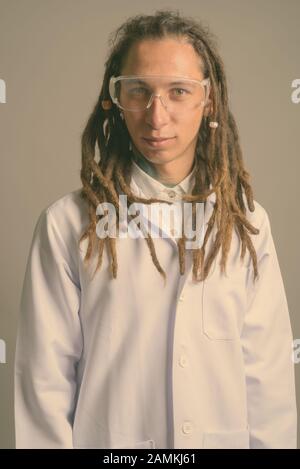 Junger Mann Doktor mit Dreadlocks trägt Schutzbrille vor grauem Hintergrund Stockfoto