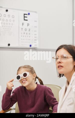 Portrait des süßen kleinen Mädchens, das während des Augenlicht-Tests in der pädiatrischen Augenheilklinik das Vision-Diagramm liest, Kopierraum Stockfoto