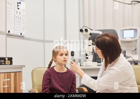 Portrait des weiblichen Optometristen mit Werkzeugen beim Überprüfen des Augenlichts des kleinen Mädchens in der modernen Klinik für Augenheilkunde, Kopierraum Stockfoto