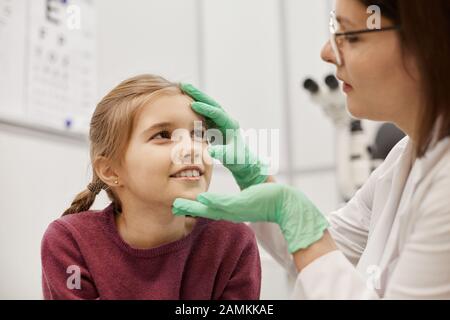 Porträt des Optometristen, der die Augen eines lächelnden kleinen Mädchens in der modernen Augenklinik überprüft, Kopierer Stockfoto
