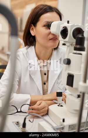 Porträt der lächelnden weiblichen Augenärztin mit Refraktometergerät während des Sehtests in der modernen Klinik Stockfoto