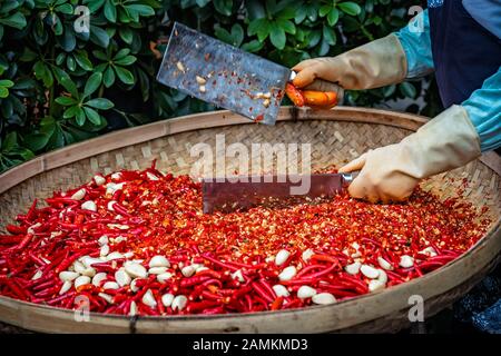 Chilis und Knoblauch werden von der Arbeiterinnen in einer Korbschale auf dem Straßenmarkt in Yangshuo, China, gehackt Stockfoto