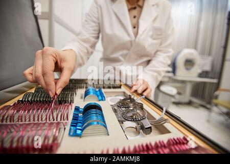 Nahaufnahme von nicht erkennbaren weiblichen Optometristen, die Objektive für den Probelahmen während der Brille wählen, die in die Klinik für ophthamologische Untersuchungen passt, Kopierraum Stockfoto