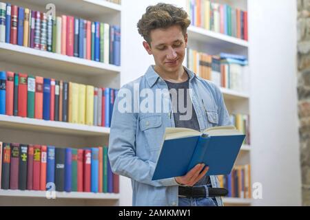 Junger Mann in der Bibliothek, der das Buch findet, das er sehr amüsant liest. Stockfoto