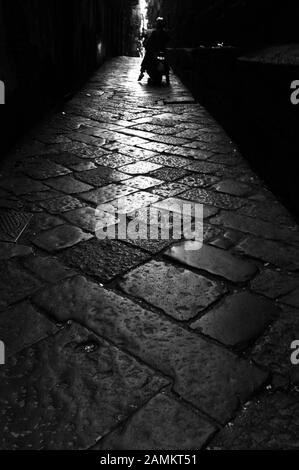 Kopfsteinpflaster in der Altstadt von Neapel. Am Ende der Gasse die Silhouette eines Motorradfahrers. [Automatisierte Übersetzung] Stockfoto