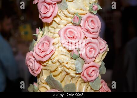 Elaborierter Hochzeitstorte aus bunter Eistrierung mit Dinosaurier-Knochen aus gelbem Eis und rosa Zuckerrosen aus Choccywocydoodah aus Brighton Stockfoto