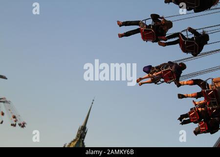 Passagiere im Kettenkarussell am Abend des Oktoberfests, auf der linken Seite des Bildes die Sternenfliegerfahrt, in der Mitte der Turmspitze von St. Paul. [Automatisierte Übersetzung] Stockfoto