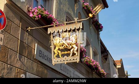 Goldenes Zunfzeichen einer Bäckerei in Bad Tölz, Krone, Löwen mit gekreuzten Schwertern und Brezel sowie drei Rollen, Balkone mit Blumenkästen, 12.10...2014, [automatisierte Übersetzung] Stockfoto