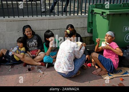 Jakarta, indonesien - 2019.12.22: Frauen und Mädchen, die auf dem Straßenbelag von Jalan kebon kacang im Stadtzentrum sitzen und Instant-Nudeln essen Stockfoto