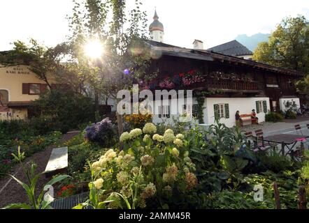 Bilderserie Garmisch-Partenkirchen: Das unter Denkmalschutz stehende alte Bauernhaus mit Bauerngarten am Mohrenplatz im Landkreis Garmisch beherbergt die öffentliche Bibliothek. [Automatisierte Übersetzung] Stockfoto