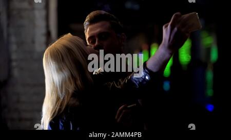 Gutaussehender Kerl, der auf dem Smartphone seinen Kuss mit der Freundin auf Party, im Nachtleben filmte Stockfoto