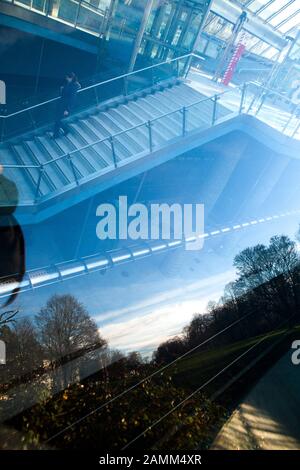 Die Grünfläche "Am hohen Weg" am U-Bahnhof St.-Quirin-Platz spiegelt sich in der Glaskuppel des Bahnhofs wider, durch die man auch die Gleise und den Bahnsteig sehen kann. [Automatisierte Übersetzung] Stockfoto