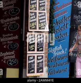 Vorstände mit Angeboten vor einem Laden in der Metzgerei am Münchner Viktualienmarkt. Die Häuserzeile mit der Sammlung von Metzgereien existiert seit 1315. [Automatisierte Übersetzung] Stockfoto