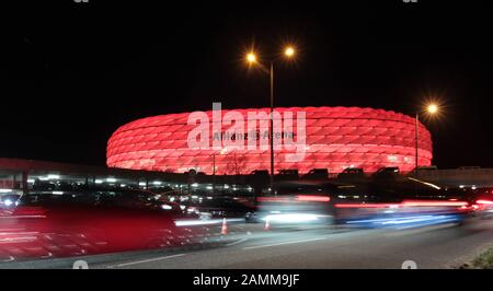 Beleuchteter Parkplatz und Licht aus vorbeifahrenden Autos in der Allianz Arena nach dem Champions-League-Halbfinale FC Bayern München - Real Madrid. Im Hintergrund die rot beleuchtete Allianz Arena. [Automatisierte Übersetzung] Stockfoto