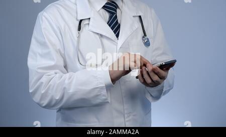 Hausarzt schreibt Nachricht auf einem modernen Smartphone und verwendet intelligente Geräte für die Arbeit Stockfoto