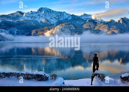 Herzogstand 1.731 m mit Kochelsee, frühmorgens, teils Nebel, Schnee auf dem Gipfel, vor der Skulptur Fischerjung - Fischer vom Kochelsee, die erstmals 1952 aus einer Drahtkonstruktion mit Putz und Ton errichtet wurde, die vom Bildhauer Prof. Richard Miller geschaffen wurde, Renoviert und vor einigen Jahren von Oswald Rifesser aus St. Ulrich in Tyrol, 10.01.2017 [automatisierte Übersetzung] Stockfoto