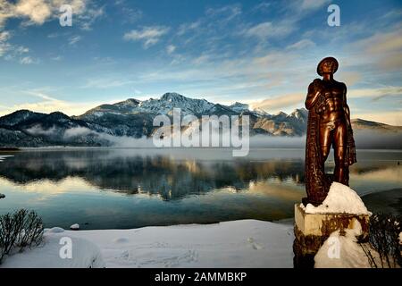 Herzogstand 1.731 m mit Kochelsee, frühmorgens, teils Nebel, Schnee auf dem Gipfel, vor der Skulptur Fischerjung - Fischer vom Kochelsee, die erstmals 1952 aus einer Drahtkonstruktion mit Putz und Ton errichtet wurde, die vom Bildhauer Prof. Richard Miller geschaffen wurde, Renoviert und vor einigen Jahren von Oswald Rifesser aus St. Ulrich in Tyrol, 10.01.2017 [automatisierte Übersetzung] Stockfoto