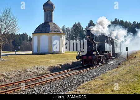 Bayerischer Lokalbahnverein Tegernsee, Federdampf, Sonderfahrt mit der Kohle-Dampflok 70 083 von 1913 von Tegernsee nach Holzkirchen und zurück, hier beim Überqueren der Bürgermeister-Erl-Straße neben der katholischen Kapelle St. Sylvester, einem sogenannten Freikirchl, in Hirschstätt bei Schaftlach, 12.03.2017 [automatisierte Übersetzung] Stockfoto