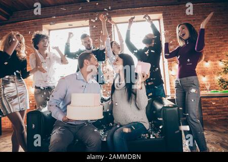 Foto der Gruppe beste Freunde überraschung Baby Party Hochzeit Jahrestag zukünftige Eltern sitzen Sofa halten großen Kuchen küssen Konfetti fallen Verschleiß formalwear Stockfoto