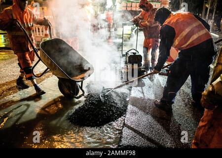 Auf einer Straßenbaustelle am Laimer Kreisverkehr (Kreuzung Landsberger / Fürstenrieder Straße) wird in der Nacht der alte Straßenbelag abgefräst und danach neuer Asphalt aufgetragen. Im Bild wird der Teer verwendet und mit einem Schubkarren gespreizt. [Automatisierte Übersetzung] Stockfoto