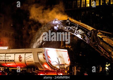 Auf einer Straßenbaustelle am Laimer Kreisverkehr (Kreuzung Landsberger / Fürstenrieder Straße) wird in der Nacht der alte Straßenbelag abgefräst und danach neuer Asphalt aufgetragen. Im Bild wird der gefräste Teer direkt auf die Ladefläche eines Staplers geworfen. [Automatisierte Übersetzung] Stockfoto