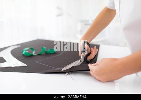 Junge Damenreißmaschine schneidet mit Scheren Detail an den Skizzenzeilen.Nahansicht Modedesigner-Hände arbeiten im Nähstudio. Maßgeschneidert Stockfoto