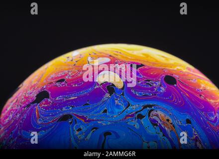 Nahaufnahme des psychedelischen Regenbogens von Farben, die sich in einer Seifenblase mischen und wirbeln, um wie eine Fantasy-Galaxie oder ein Planet zu aussehen, der einen schwarzen Hintergrund isolierte Stockfoto