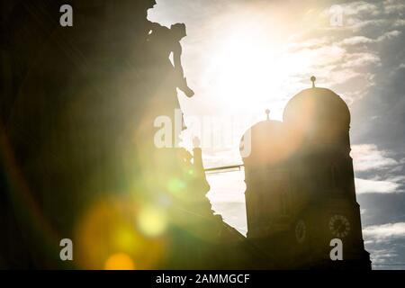 Die Türme des Liebfrauendoms in der Abendsonne, fotografiert von der Kardinal-Faulhaber-Straße. Die Statue im Vordergrund steht auf dem Dach der Bayerischen Hypotheken- und Wechselbank. [Automatisierte Übersetzung] Stockfoto