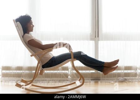 Entspannte afrikanerin, die auf einem Holzschaukelstuhl ruht Stockfoto