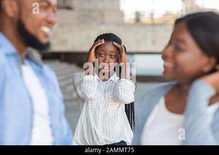 Verärgerte schwarze Frau, die beobachtet, wie ihr Freund draußen mit anderen Mädchen flirtet Stockfoto