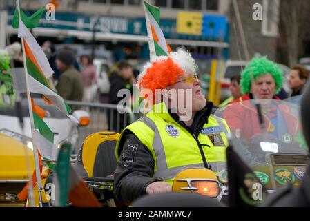 Ein erwachsener Biker mit der irischen Tricolor Perücke auf einem Motorrad, der am 17. März 2019 an der jährlichen St. Patrick's Day Parade in Killarney, County Kerry, Irland, teilnimmt. Stockfoto