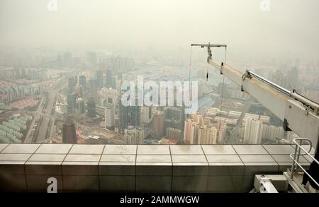 Dach des Wolkenkratzers mit Wartungskran für die Fensterreinigung. Vogelblick auf moderne Gebäude in Shanghai teilweise versteckt durch verschmutzte Luft Stockfoto