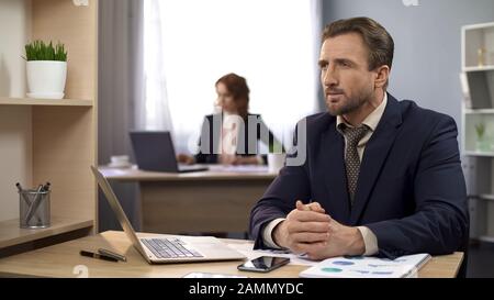 Mann im Geschäft sitzt am Schreibtisch und denkt über Einkommen, Arbeitsplatz nach Stockfoto