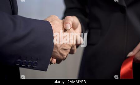Top-Manager schüttelt nach dem Bandschneiden die Hände mit weiblichem Geschäftspartner Stockfoto